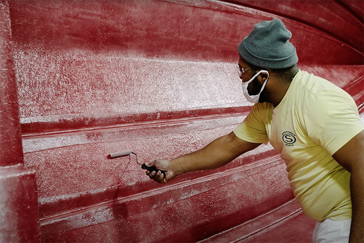 Image of Sportsman Boats employee using a bubble roller to press air from between layers of fiberglass and resin in a boat hull.