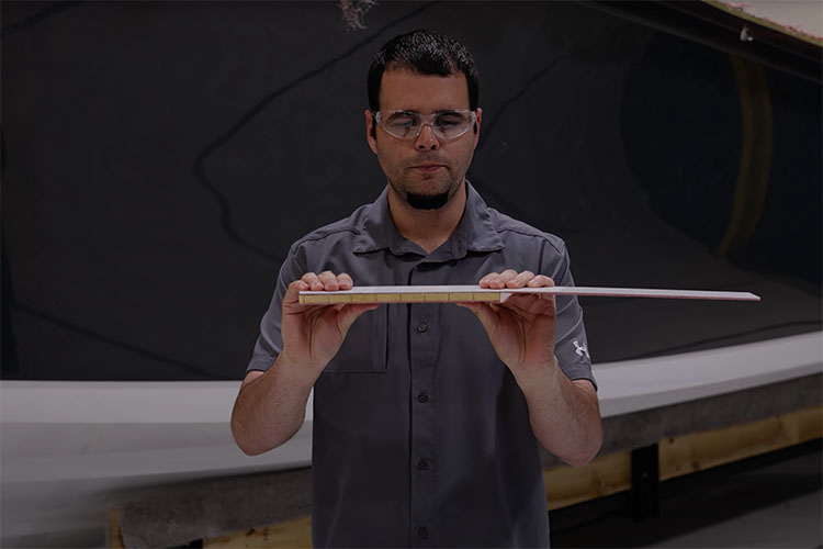 Image of Sportsman Boats employee demonstrating the strength of coring board by comparing the bend in plain fiberglass to fiberglass backed with coring foam