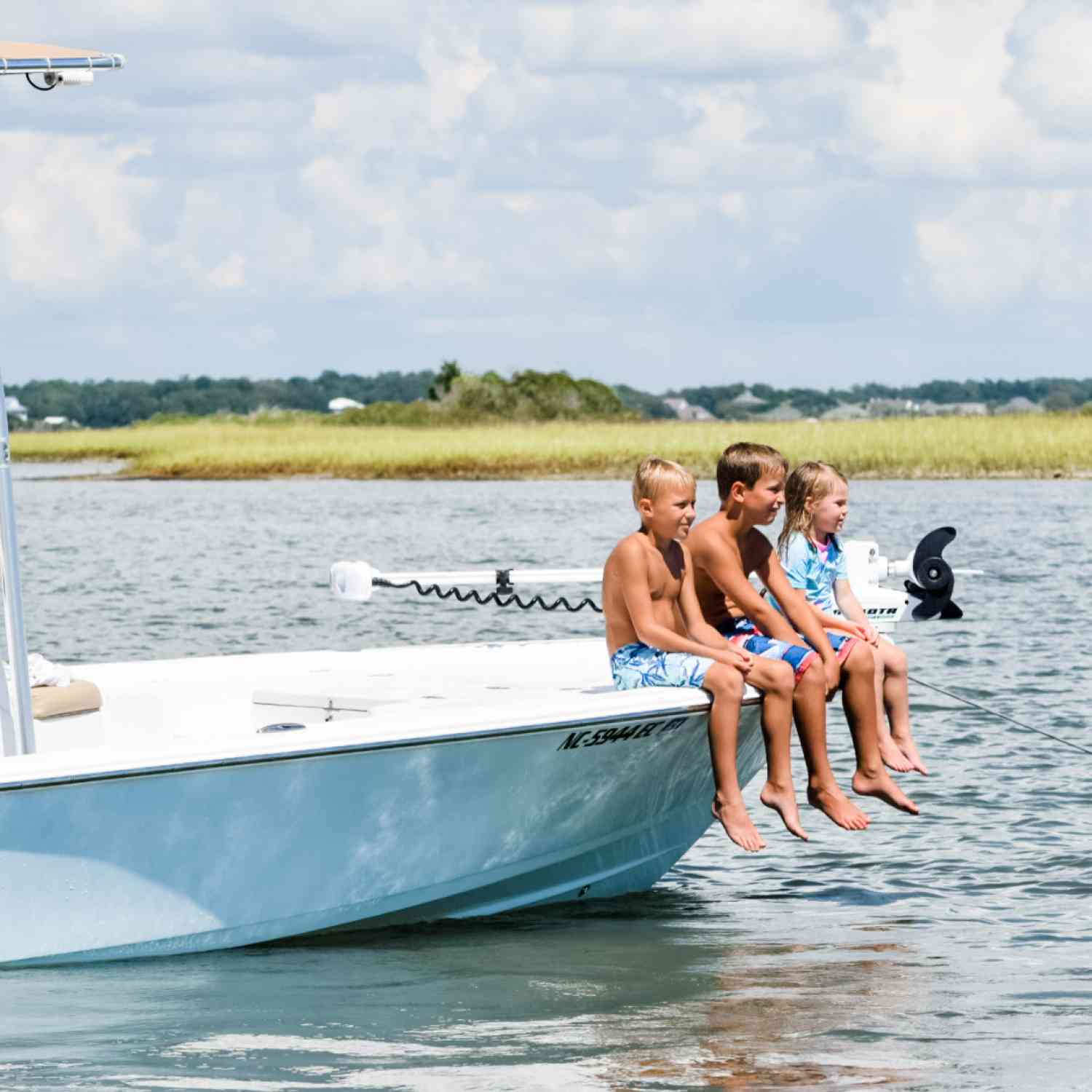 Brother, sister and cousin sitting on the edge of the boat watching the dolphins swim by.